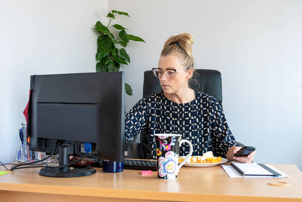 attractive middle-aged woman with eyeglasses at noon in the office at the desk - Foto, Bild