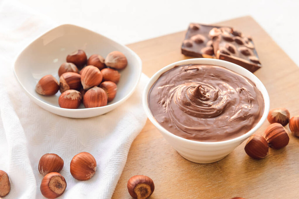 Bowl with tasty chocolate paste and hazelnuts on light background - Photo, Image