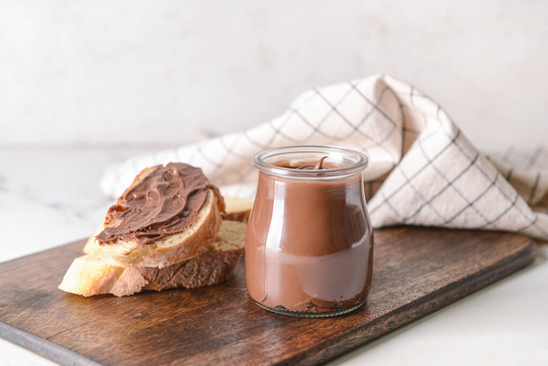 Frasco com pasta de chocolate saborosa e avelãs no fundo claro - Foto, Imagem