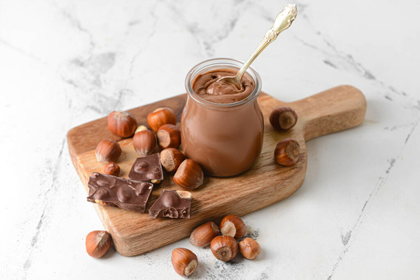 Jar with tasty chocolate paste and hazelnuts on light background - Photo, Image