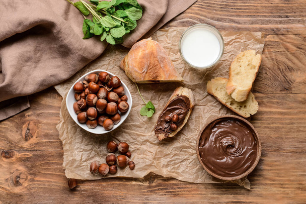 Bowl with tasty chocolate paste and hazelnuts on wooden background - Photo, Image