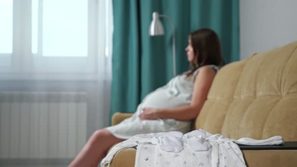 Zbliżenie ubrań noworodków na niewyraźne tło kobiety w ciąży - Materiał filmowy, wideo