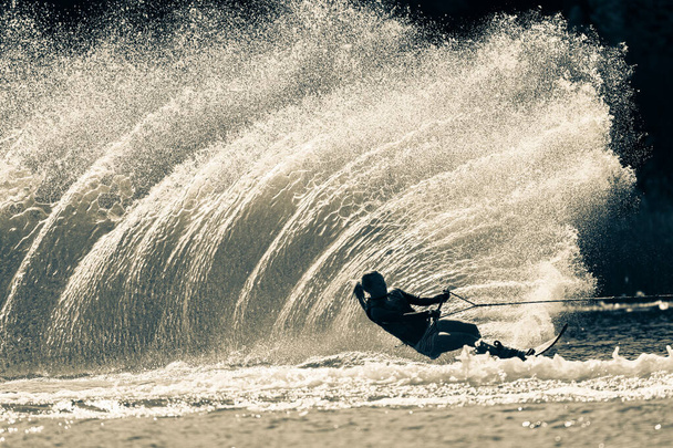Water ski girl unrecognizable athlete skiing slalom carves a vertical water wake spray  in vintage sepia black white tone for a dramatic contrasts action photograph. - Photo, Image