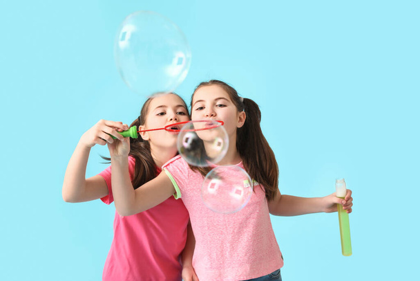 Nette Zwillingsmädchen blasen Seifenblasen auf farbigem Hintergrund - Foto, Bild