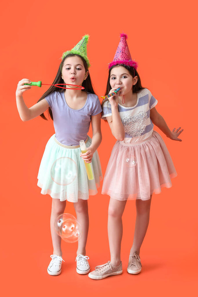 Cute twin girls in party hats blowing soap bubbles on color background - Foto, Bild