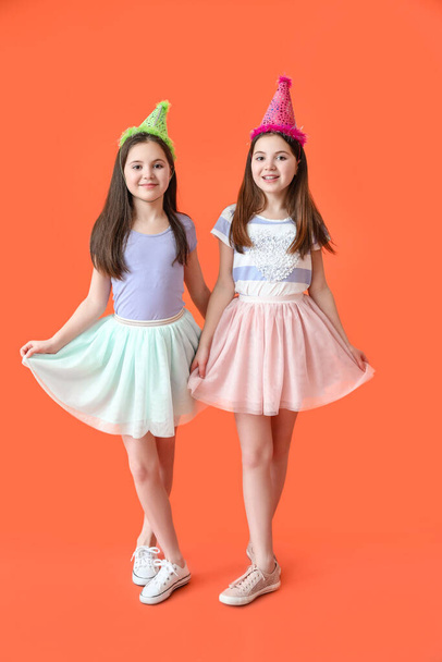 Nette Zwillingsmädchen in Party-Hüten auf farbigem Hintergrund - Foto, Bild