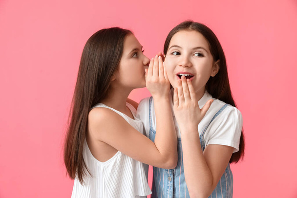 Little girl telling sister her secret on color background - Foto, Imagem