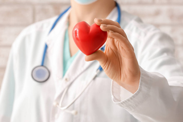 Cardiologa femminile con cuore rosso vicino al muro di mattoni, primo piano - Foto, immagini