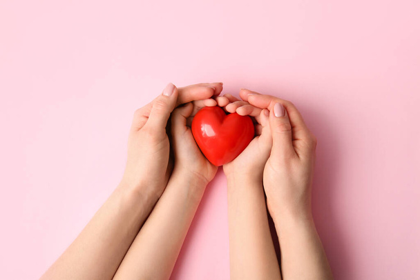 Hands of woman and child with red heart on color background - Photo, Image