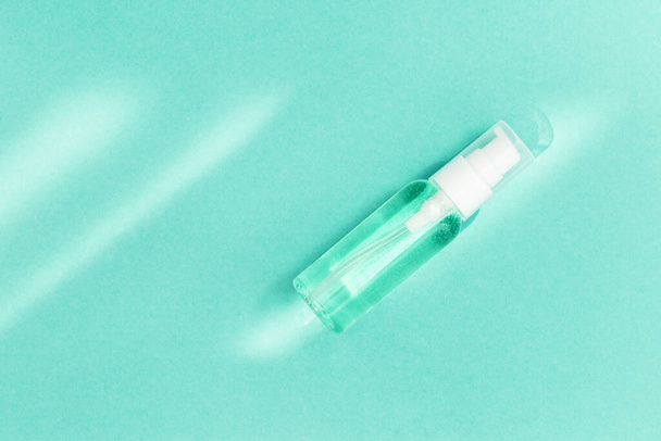 Small bottle with transparent cosmetic product, gel or crem on mint colored background. Flack with moisturizer for self-care. Monochrome image. - Fotografie, Obrázek