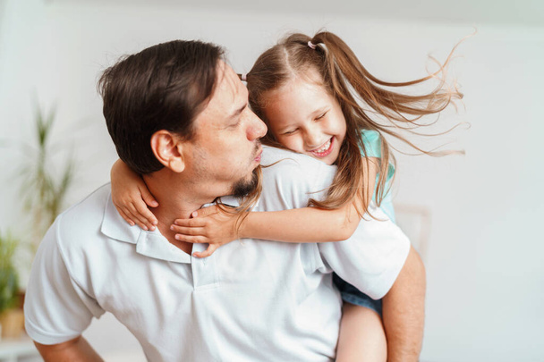 Χαρούμενος χαρούμενος χαρούμενος μπαμπάς παίζει με τη μικρή γοητευτική κόρη του στο σπίτι. Ο άντρας κάνει κύκλους και ξερνάει το κορίτσι. Μια δυναμική εικόνα. Αντιγραφή χώρου - Φωτογραφία, εικόνα