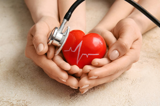 Handen van vrouw en kind met rood hart en stethoscoop op grunge achtergrond, close-up - Foto, afbeelding