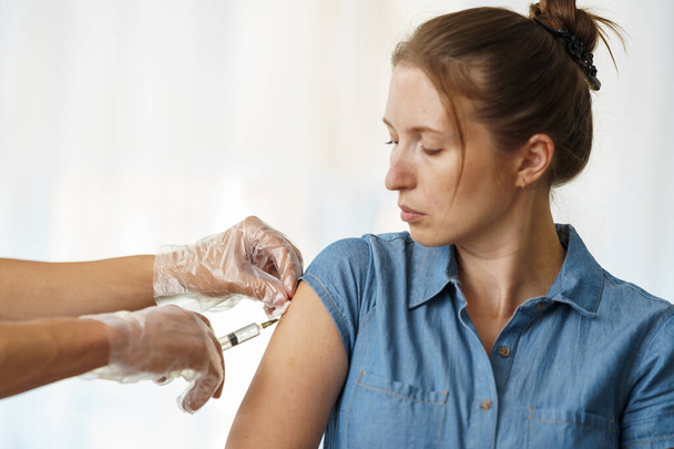 doctor gives an adult young woman an injection in shoulder. Vaccination of adults against coronavirus. vaccine against Covid-19. Protection against the virus. Close up. copy space - Photo, Image