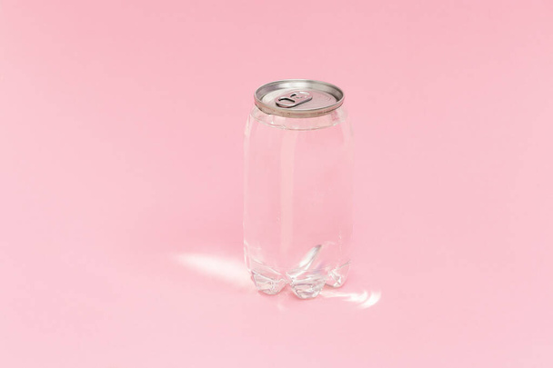 Transparent can of water with sunlight on pink background. Monochrome image. Creative idea, new package of clear water in plastic bottle as can. - Photo, Image