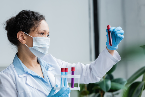 African american scientist in medical mask looking at test tube with sample  - Fotó, kép