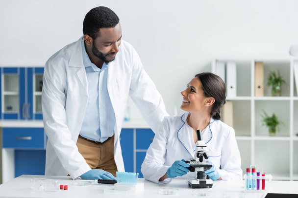 Bilim adamları mikroskop ve test tüplerinin yanındaki Afrikalı Amerikalı meslektaşlarına gülümsüyor.  - Fotoğraf, Görsel