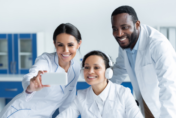 Cheerful multiethnic doctors using blurred smartphone in clinic  - Photo, Image