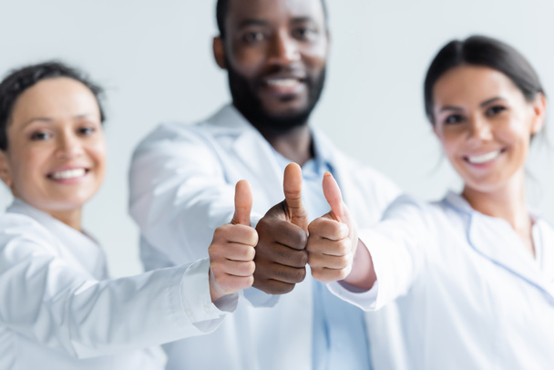 Interraciale artsen op wazig achtergrond tonen duimen omhoog  - Foto, afbeelding