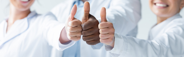 обрезанный вид размытых многонациональных врачей, показывающих большие пальцы вверх, баннер  - Фото, изображение