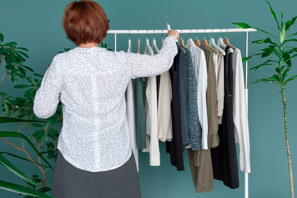 Mujer de mediana edad hace compras y mira el nuevo vestido cerca de estante con ropa. - Foto, imagen