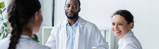 African american doctor smiling to colleague in clinic, banner  - Фото, зображення