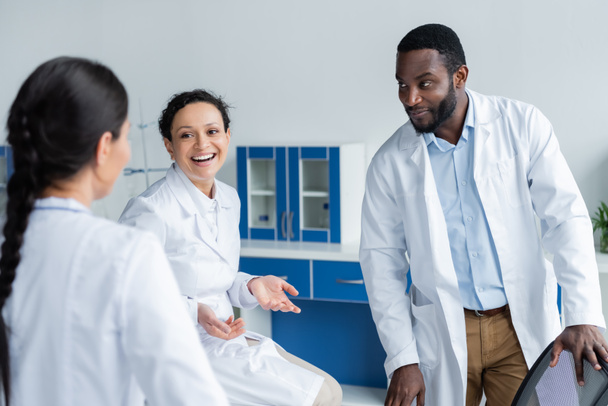 Cheerful african american doctor talking to colleagues in hospital  - Fotó, kép