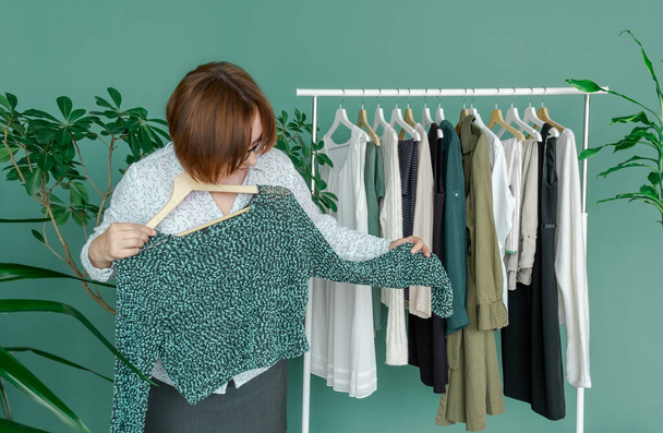 Middle Aged Woman makes shopping and looks at the new dress near shelf with clothes. - Foto, Bild