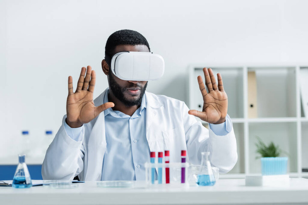 African american scientist in vr headset sitting near blurred medical equipment - Photo, Image