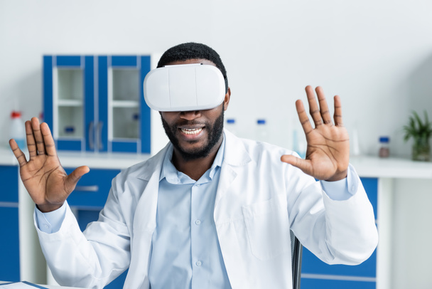 улыбающийся африканский американский врач в наушниках виртуальной реальности в клинике  - Фото, изображение
