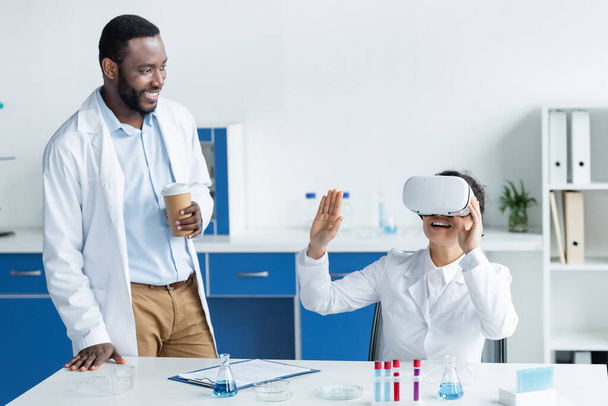 Fröhliche afrikanisch-amerikanische Wissenschaftler mit vr-Headset und Kaffee im Labor  - Foto, Bild