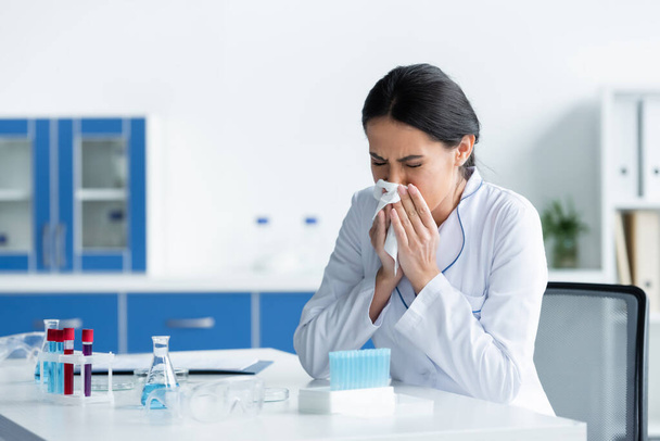 Naukowiec z serwetką kichającą w pobliżu sprzętu medycznego w laboratorium  - Zdjęcie, obraz
