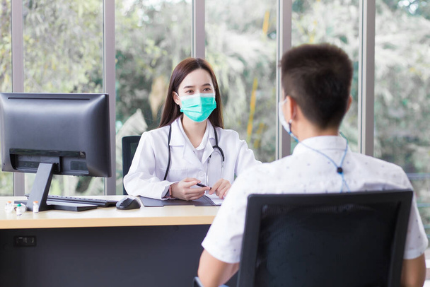 Azji profesjonalny lekarz nosi płaszcz medyczny i maskę twarzy podczas badania i rozmowy z mężczyzną pacjenta w pokoju badań w szpitalu. - Zdjęcie, obraz