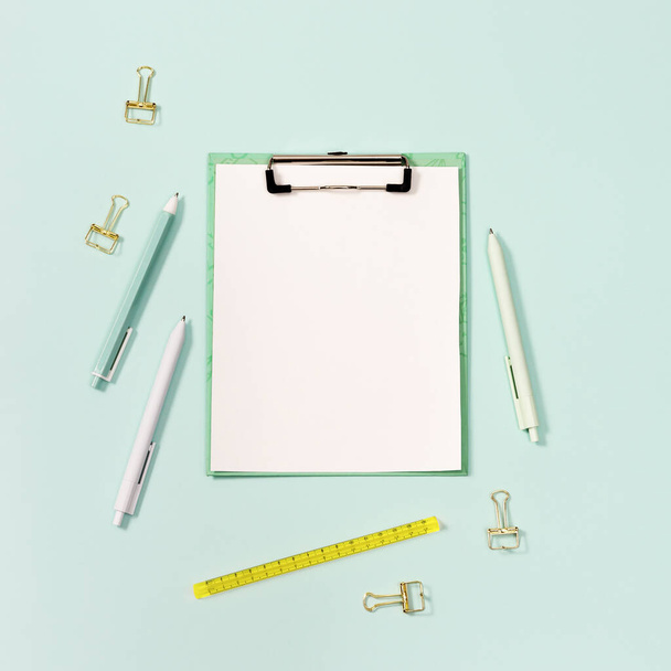 Paper tablet with clip and stationery. Back to school concept. Blue and white colored pens, yellow ruler and modern paper clips. View from above and mock up. - Photo, Image