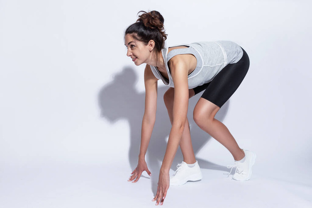 Young woman in sportswear at a low start. Beautiful slender brunette. White background. Active lifestyle. - Photo, image