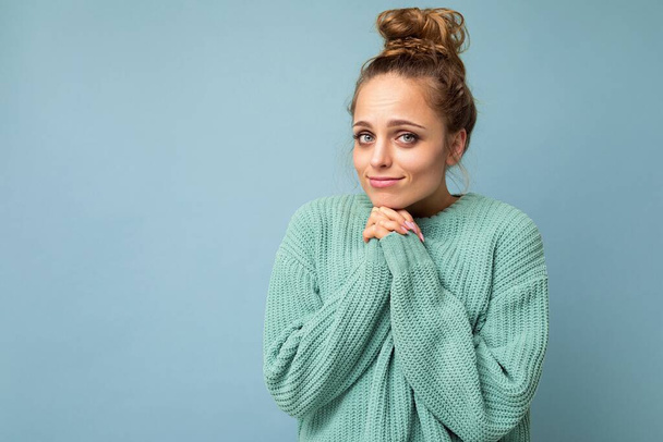 Photo of young positive beautiful blonde woman with sincere emotions wearing casual blue pullover isolated over blue background with copy space holding hands together - Photo, Image