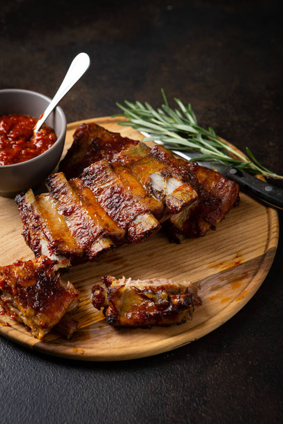 Close up of barbecue smoked ribs with red sauce on wooden plate - Foto, Bild