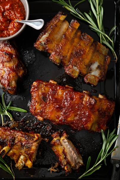 Overhead view of barbecue smoked ribs with red sauce on black surface - Photo, Image