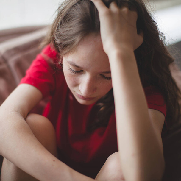 Sad teen girl sits on Sofa feels depressed, offended or lonely, upset young woman suffers from abuse, harassment or heartbreak, grieving lady or violence victim has psychological problem - Fotó, kép