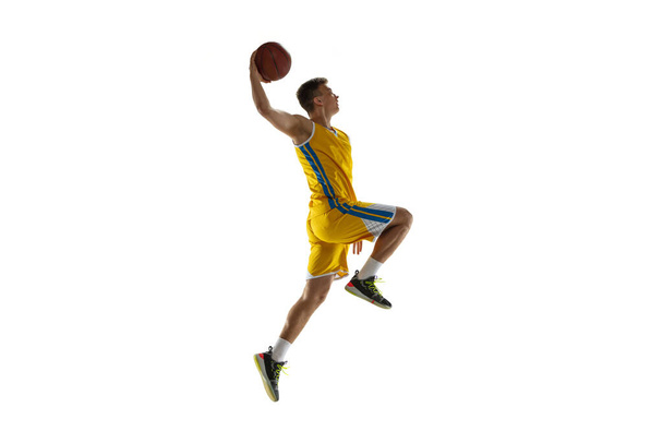 Side view. One young man, basketball player with a ball training isolated on white studio background. Advertising concept. Fit Caucasian athlete jumping with ball. - Photo, Image