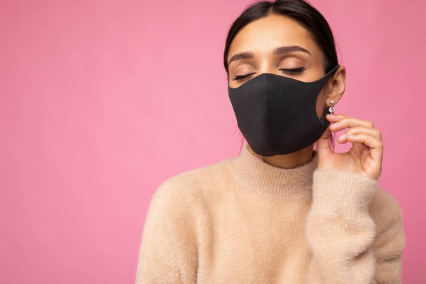 Mujer hermosa joven en la máscara protectora del virus reutilizable en la cara contra el coronavirus aislado en la pared de fondo rosa - Foto, imagen