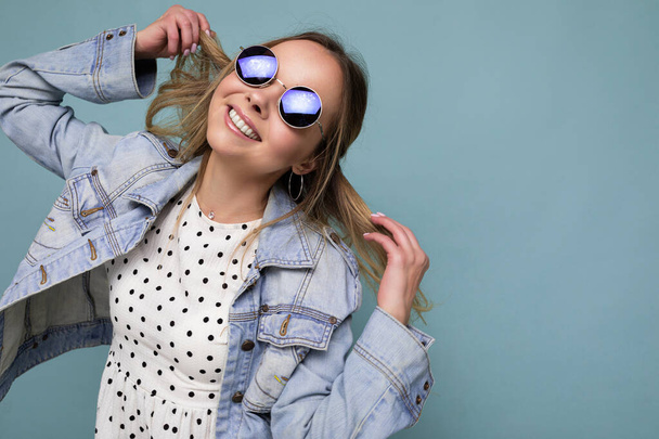 Foto de atractiva mujer rubia sonriente feliz usando ropa casual de verano y gafas de sol con estilo aislado sobre la pared de fondo colorido mirando a un lado y divertirse - Foto, Imagen