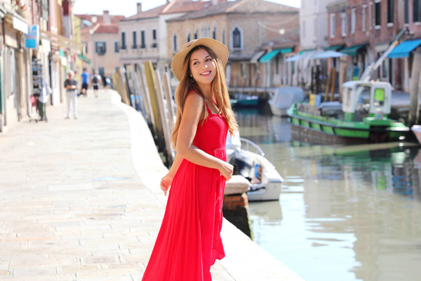 Fashion. Smiling young stylish woman looking back walking in the old town of Murano in Venice, Italy. - Photo, Image