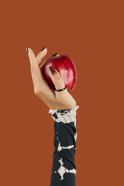 Las mujeres de la mano con la manicura marrón de moda que sostiene la manzana. Diseño de uñas de otoño - Foto, imagen