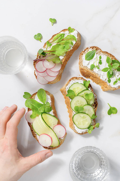 Hand streckt Sandwiches mit Weichkäse, Rettich und Gurke - Foto, Bild
