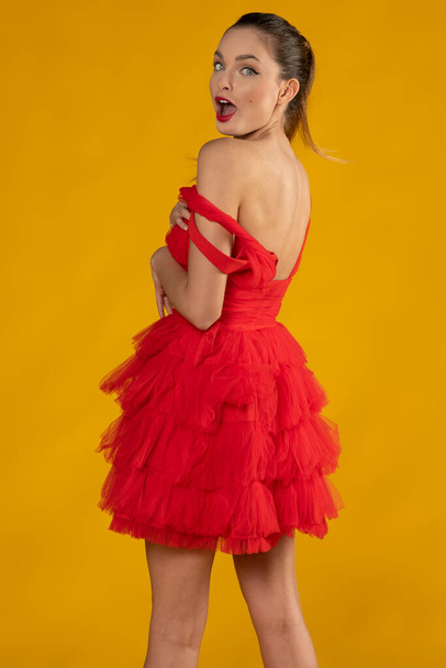 attractive sexy pin-up showing her shoulder , and making face she is dressing a pretty red toulle, and looking in camera posing on yellow - Fotó, kép