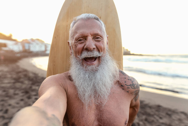 Surfista sênior feliz tirar selfie enquanto se diverte surfando ao pôr do sol - Vida de pessoas idosas saúde e conceito de esporte extremo - Foto, Imagem