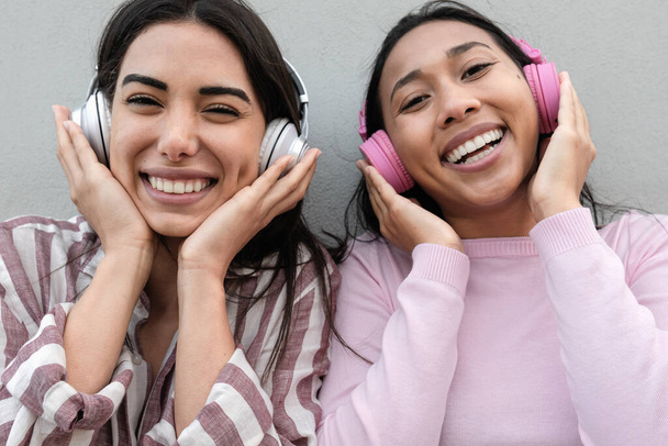 Молодые счастливые латиноамериканские девушки с удовольствием слушают музыку в беспроводных наушниках на открытом воздухе - Фото, изображение