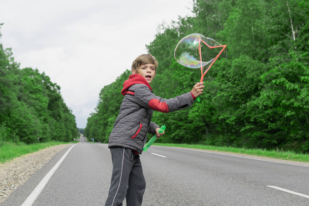 A little boy is playing on a highway outside the city, blowing soap bubbles - Fotografie, Obrázek