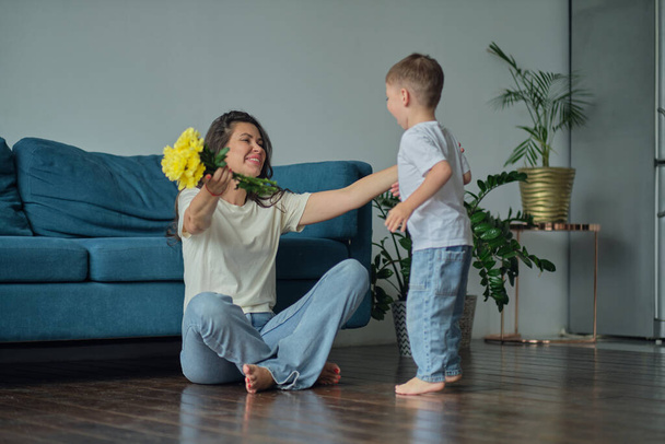 Happy mother day. child son congratulates mother on holiday and gives flowers. congratulating her on mothers day during holiday celebration at home - Фото, изображение