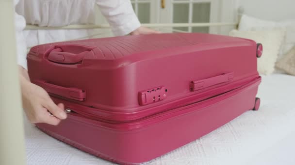 Μια γυναίκα κλείνει στο κρεβάτι μια μεγάλη ροζ βαλίτσα με ρούχα. - Πλάνα, βίντεο
